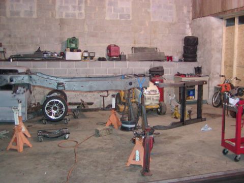 1991 Ford Bronco - Vehicle frame undergoing work in a garage setting, surrounded by tools and equipment.