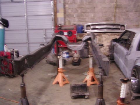 1991 Ford Bronco - The chassis of a vehicle is supported by jack stands in a workshop setting.