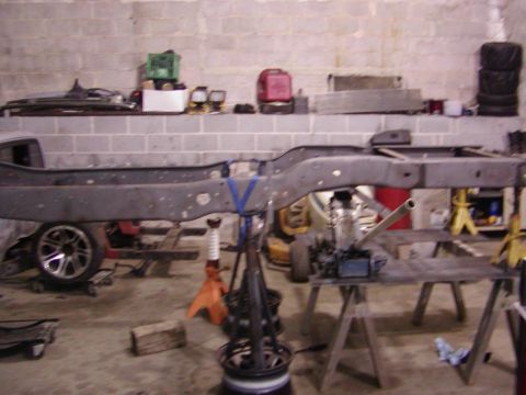 1991 Ford Bronco - A vehicle frame is suspended on jack stands in a garage setting.