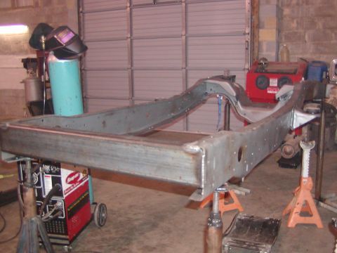1991 Ford Bronco - A vehicle frame is supported by jack stands in a workshop, with welding equipment visible.