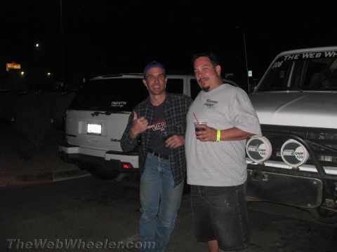 1990 Ford Bronco - Two men pose for a photo at night in a parking lot in front of parked SUVs, one giving a shaka hand sign.