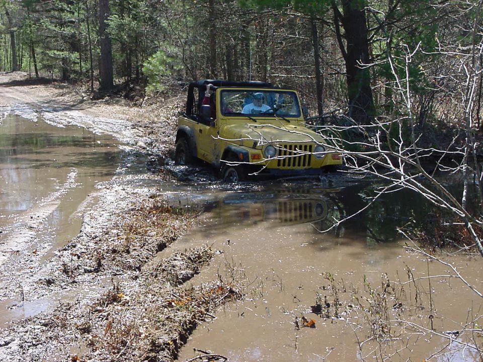 Yellow Jeep Wrangler driving through a muddy puddle off-road