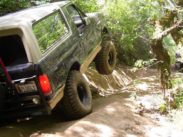Dark Ford Bronco SUV climbing a rutted dirt trail with lifted front tire off-road