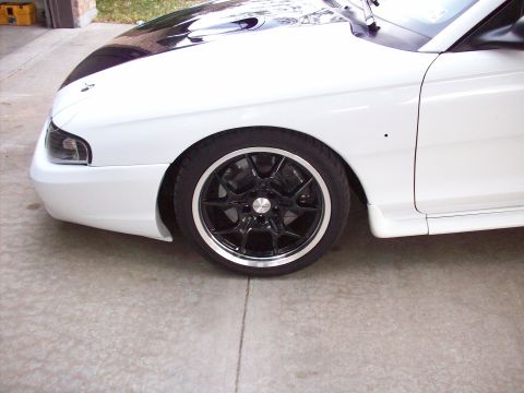 1997 Ford Mustang - Close-up of the front passenger side wheel and fender of a white 1997 Ford Mustang.