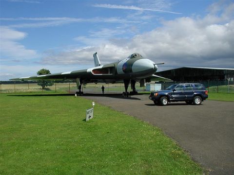 1991 Ford Crown Victoria - A blue SUV is parked on a tarmac next to a large jet aircraft on display at an airfield.