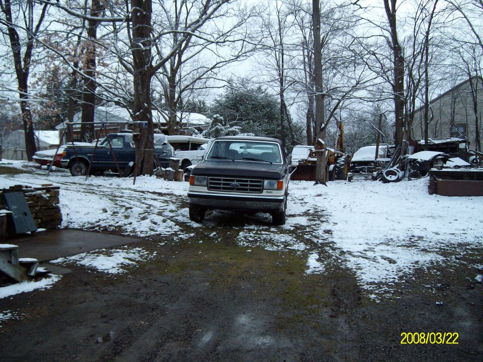 Dark pickup truck with a chrome grille and white trim, parked in a snowy yard