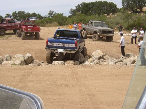 1989 Ford Bronco - A lifted blue Chevrolet pickup truck navigates a rocky obstacle course with other vehicles and spectators present.