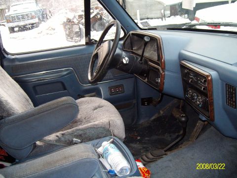 1988 Ford Bronco - Driver-side interior of a blue Ford truck shot from the passenger seat, showing the blue dash with woodgrain-trim gauge cluster and radio b…