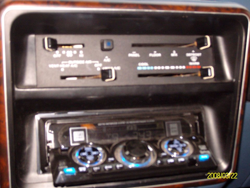 Dashboard HVAC slider controls above an aftermarket stereo with blue-lit knobs.