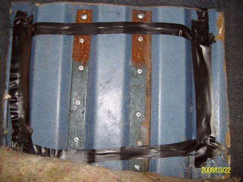 1988 Ford Bronco - Overhead view of a cut rectangular access hole in a ribbed blue-painted floor pan, with the carpet and jute padding pulled back and the cut…