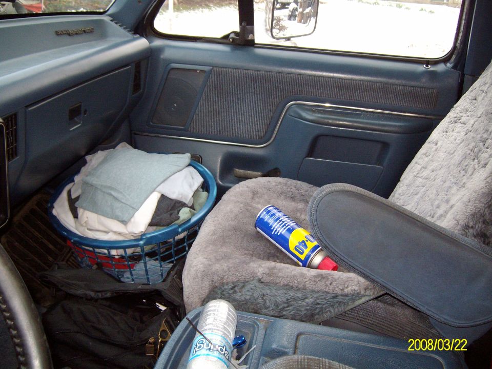 Blue Ford truck interior with sheepskin seat cover, WD-40 can and laundry basket of rags