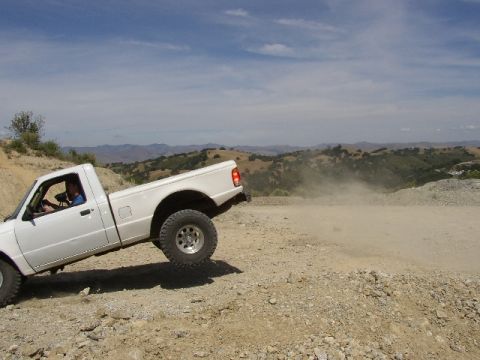1989 Ford Bronco - White pickup truck navigates a dusty off-road trail with hills in the background.