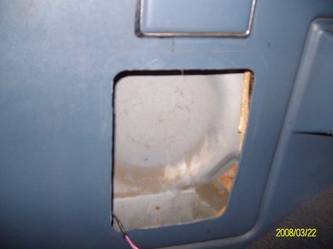 1988 Ford Bronco - Close-up of a blue interior trim panel with a square opening cut for a speaker, exposing the painted white sheet metal and surface rust beh…