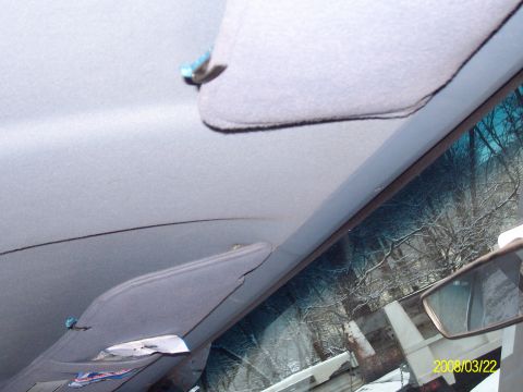 1988 Ford Bronco - Interior view looking up at a gray cloth headliner with two folded sun visors and their blue-tipped clips, plus the windshield header trim.…
