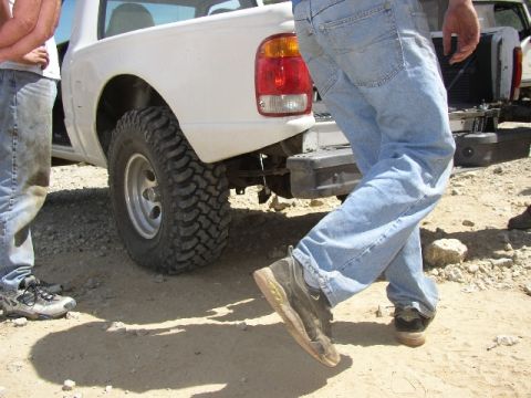1989 Ford Bronco - A white pickup truck is parked on a dirt lot with two people standing nearby.