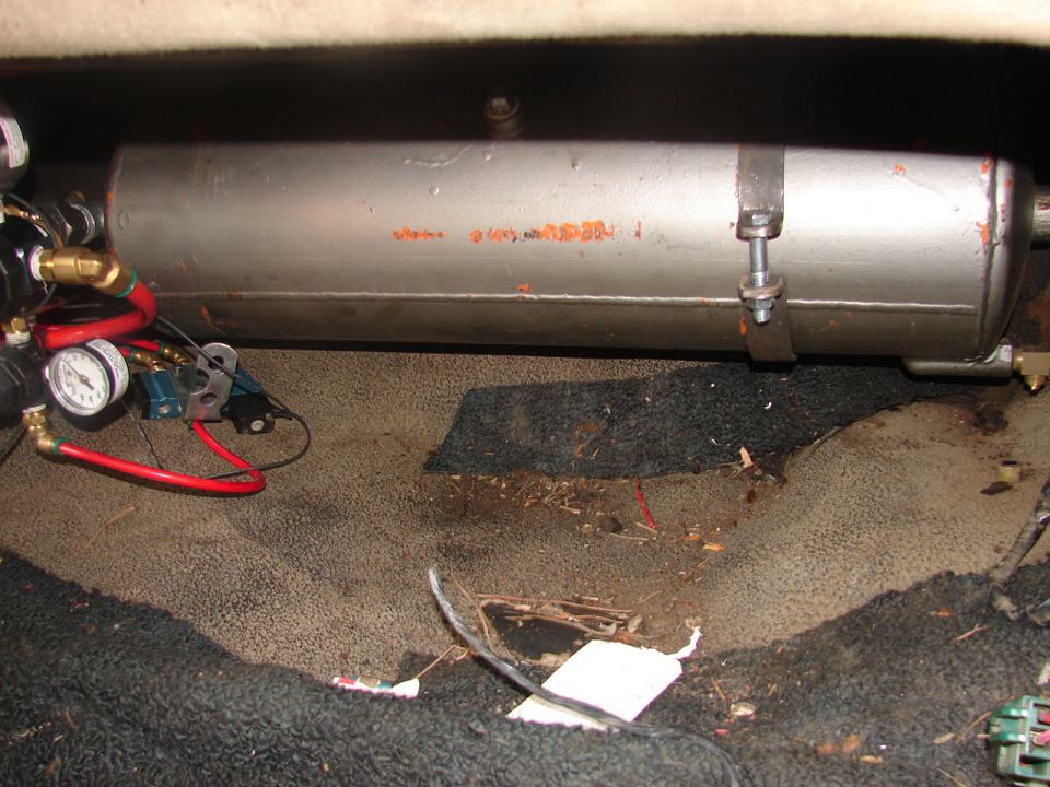 Silver onboard air tank with pressure gauge, brass fittings and red air lines mounted over trunk carpet