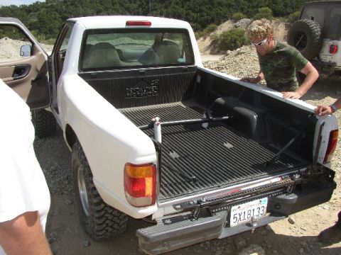 1989 Ford Bronco - Rear view of a white pickup truck with its tailgate down, parked outdoors with another vehicle in the background.