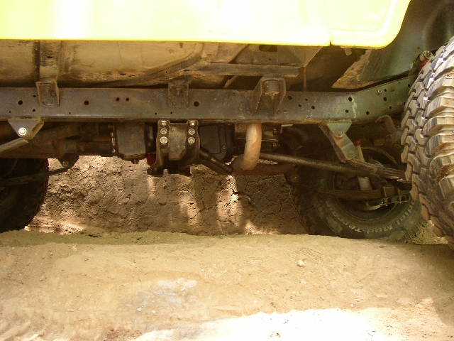 Undercarriage of yellow SUV showing frame, suspension and mud tire over dirt