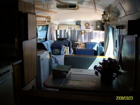 1988 Ford Bronco - Interior of a school bus converted to a motorhome, looking forward from the rear kitchen area past a dinette table with placemats and a vas…