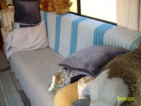 1988 Ford Bronco - Sleeping and lounge area inside a converted bus or RV: a light gray bench sofa/bed against the wall below a curtained side window, draped w…