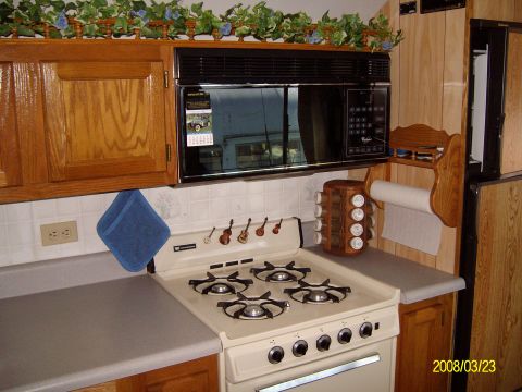 1988 Ford Bronco - Galley kitchen inside a converted bus or RV with an almond four-burner gas range and oven set into gray countertop, a black over-range Whir…
