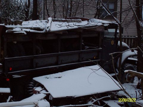 1988 Ford Bronco - An old military truck sits abandoned in the snow, its wooden bed covered by a makeshift tarp.