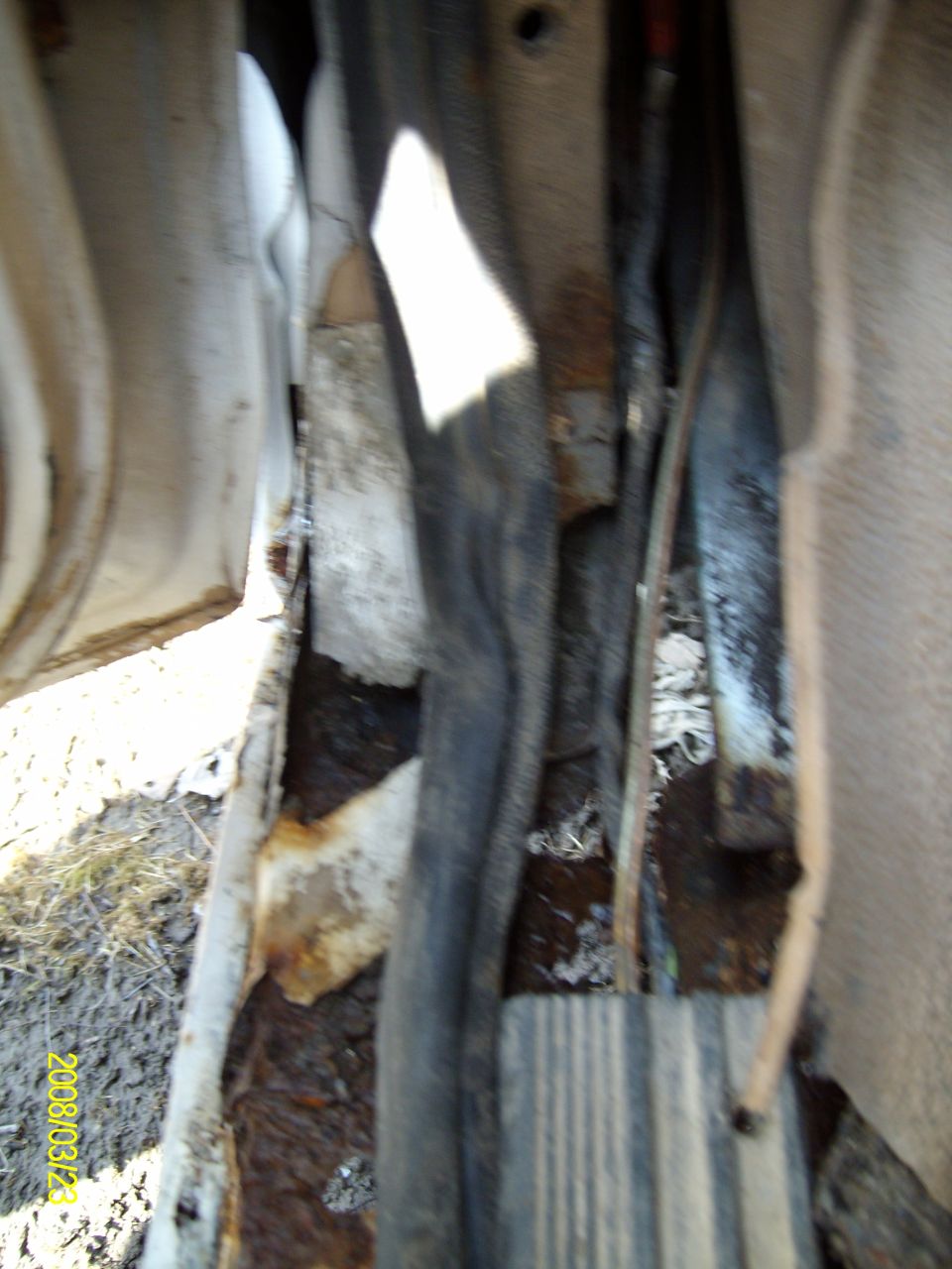 Blurry close-up of rusted-through floor pan and door sill with weatherstrip on a truck, date stamped 2008/03/23