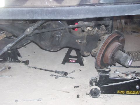 1988 Ford Bronco - The rear axle and suspension of a vehicle are disassembled, with various tools and equipment supporting the components.