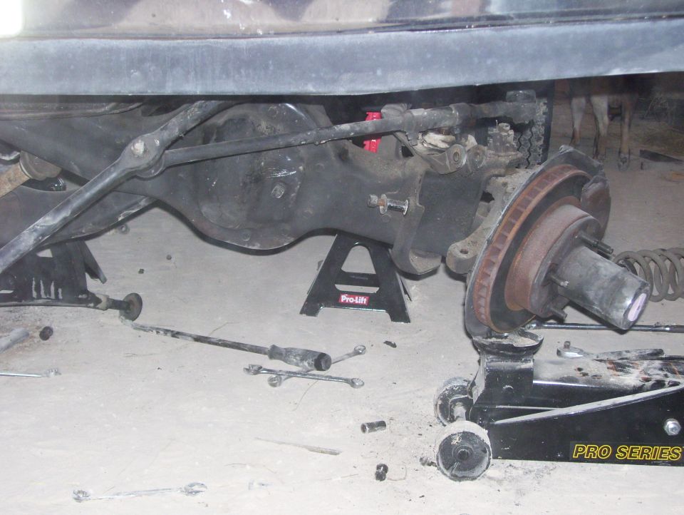 rear axle and suspension parts on jack stands and a floor jack, with tools scattered around