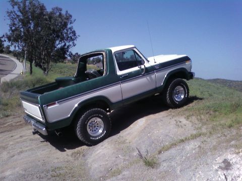 1978 Ford Bronco - A two-tone green and white 1978 Ford Bronco is parked on a dirt hill under a clear blue sky.