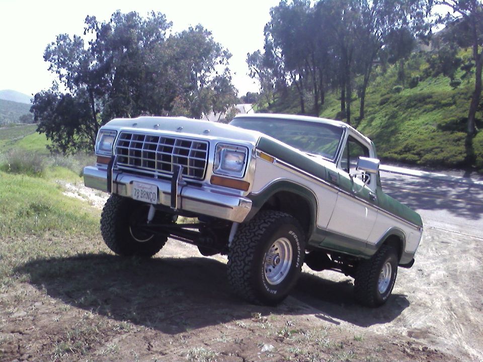 1978 Ford Bronco with white and green paint, lifted suspension, and off-road tires parked on a dirt incline