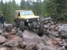 1991 Ford Bronco - A yellow Jeep Wrangler navigates a challenging rocky trail in a wooded area.