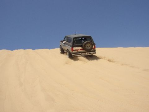 1989 Ford Bronco - Ford Bronco navigates a sandy incline under a clear blue sky.