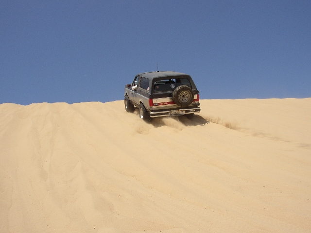 Gray Ford Bronco SUV climbing a sand dune, rear view with spare tire