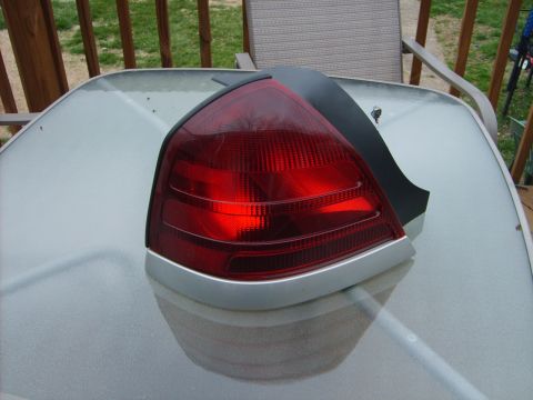 1993 Ford Crown Victoria - A single taillight assembly is shown on a glass table, with a wooden fence and grass in the background.