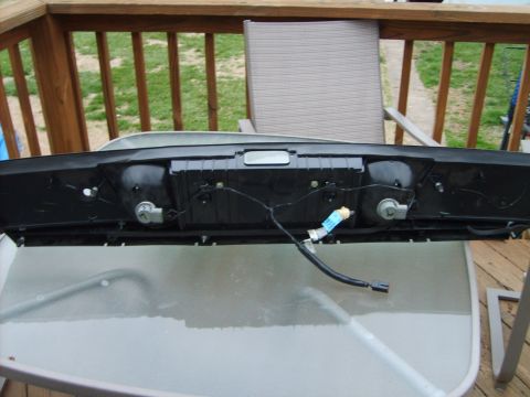 1993 Ford Crown Victoria - Back side of a rear center trim/finish panel standing on a glass patio table, showing the black plastic housing with backup-light bulb sock…