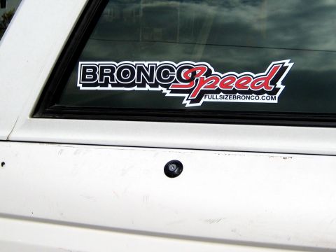 1996 Ford Bronco - Close-up of a BroncoSpeed decal with red script lettering and the FULLSIZEBRONCO.COM web address applied to the tinted rear glass of a whit…