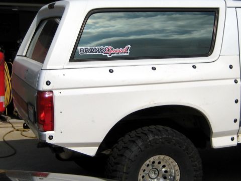 1996 Ford Bronco - Rear quarter view of a white full-size Ford Bronco SUV showing the tailgate area, taillight, rear side window, and a large off-road tire on…