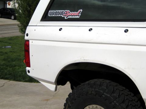 1996 Ford Bronco - Close-up of the driver-side rear quarter of a white Ford Bronco with a BroncoSpeed / FullSizeBronco.com sticker in the quarter window. The…