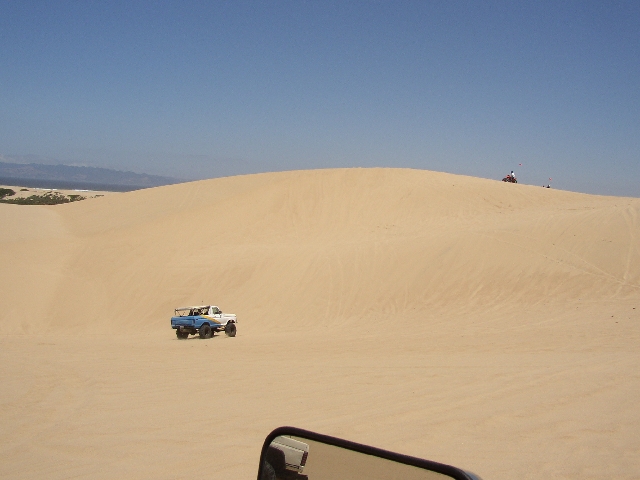 White and blue truck driving on sand dunes under clear blue sky