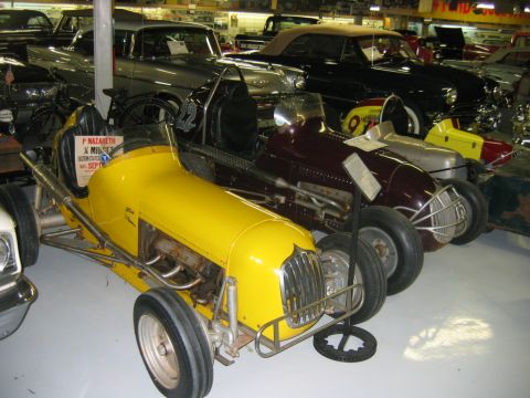 1992 Ford Mustang - Several vintage midget race cars are displayed in a museum setting, with other classic vehicles visible in the background.