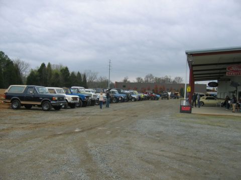 1992 Ford Mustang - A collection of Ford Broncos and other trucks are parked in a lot outside a dealership, under a cloudy sky.