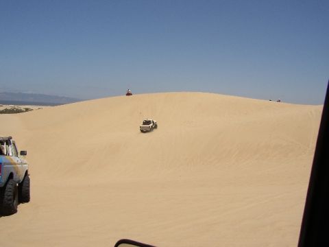 1989 Ford Bronco - Off-road vehicles navigate sandy terrain on a bright, sunny day.