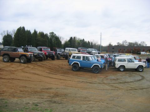 1992 Ford Mustang - A collection of Ford Broncos are gathered on a dirt lot under an overcast sky.