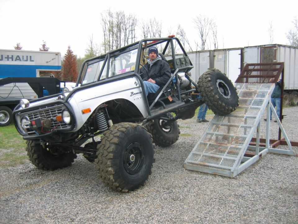 Modified Ford Bronco with roll cage and large tires on a ramp