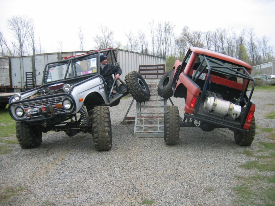 Silver and red modified SUVs with roll cages and large tires on a gravel lot