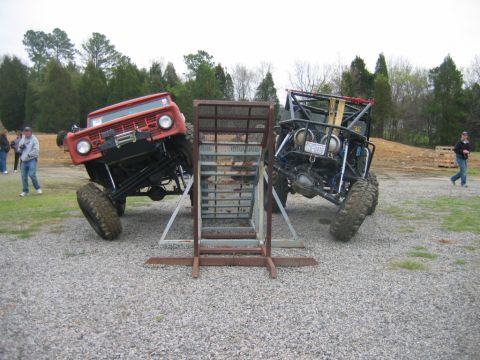 1992 Ford Mustang - Two heavily modified off-road vehicles navigate an obstacle course, one a red Bronco-style vehicle and the other a custom buggy.