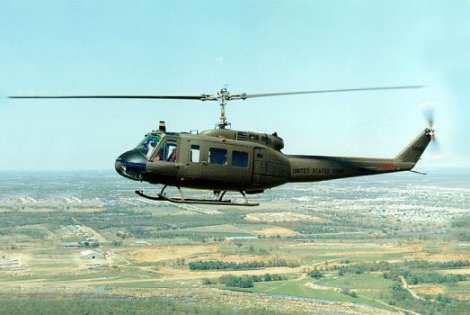 1986 Ford Bronco - A Bell UH-1 Iroquois helicopter, also known as a Huey, flies over a landscape. "UNITED STATES" is marked on its tail.