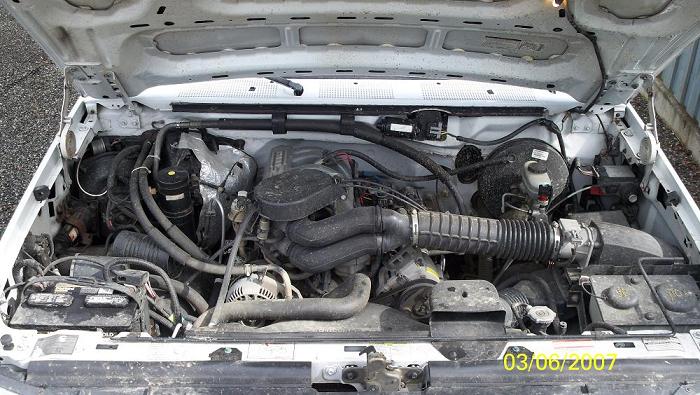 Engine bay of a white 1992 Ford F-150 with the hood open, showing the V8 engine and various components