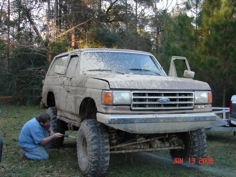 1987 Ford Bronco - Muddy 1987 Ford Bronco being cleaned after off-roading, with a person washing the front wheel.